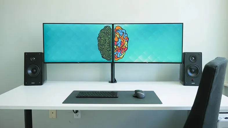 Clean dual‑monitor workstation with a split brain graphic, representing both technical and creative aspects of web app testing.